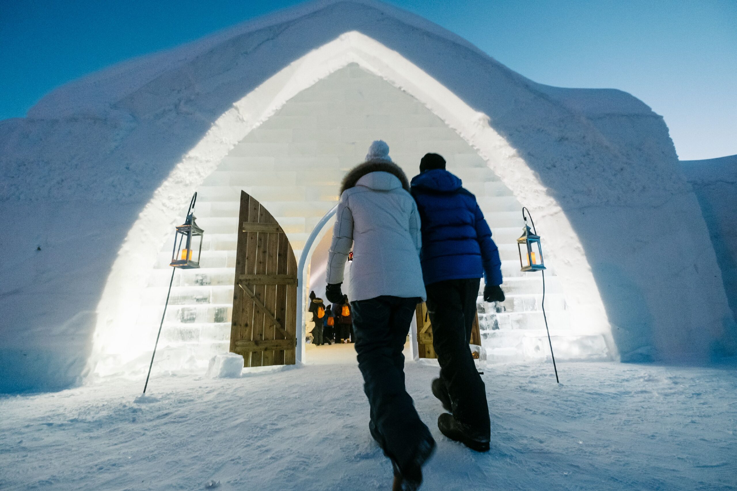 Casal de mãos dadas à entrada do Hôtel de Glace, entre lanternas e paredes de gelo
