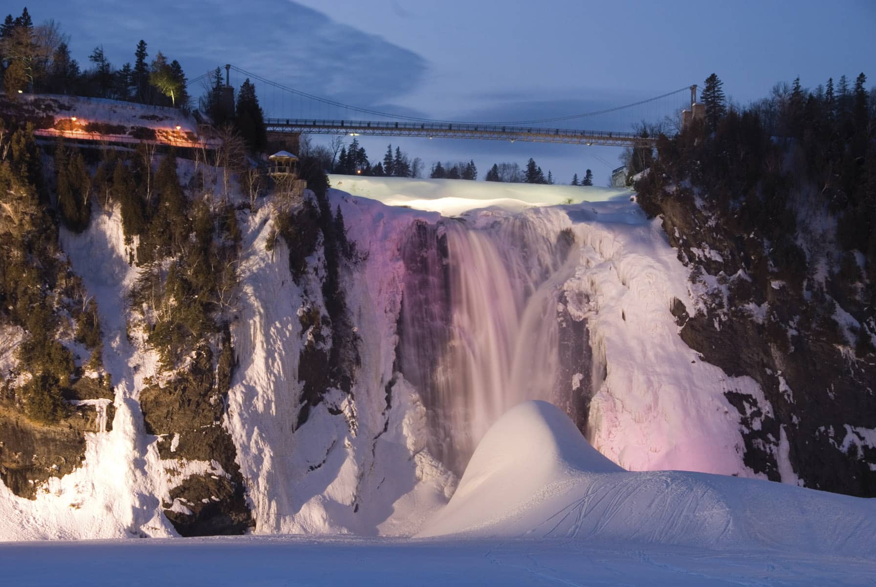 Cascata de Montmorency parcialmente gelada e iluminada ao anoitecer, com ponte suspensa