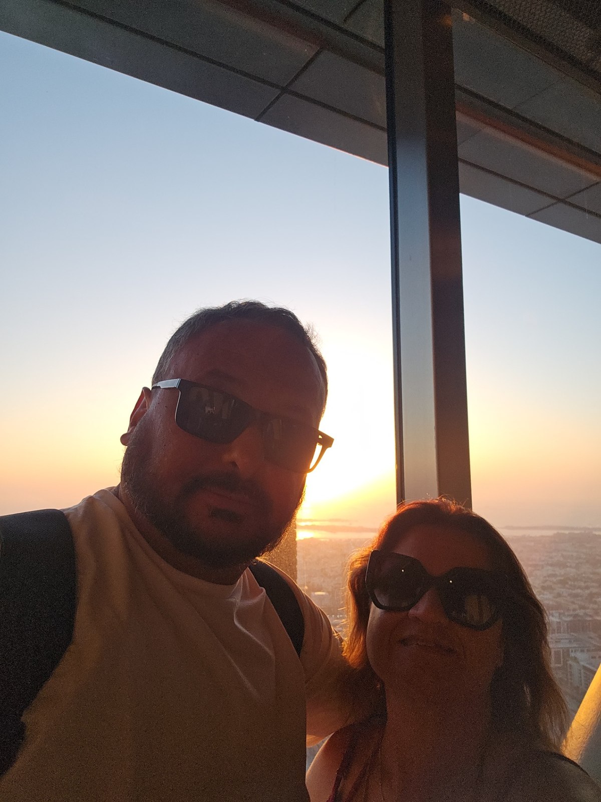 Marilene e Hugo junto ao vidro do miradouro ao pôr do sol